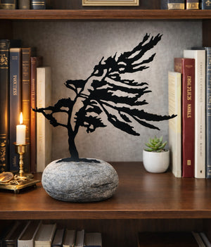 Decorative metal tree sculpture on a stone base in a home office setting with books and a candle.